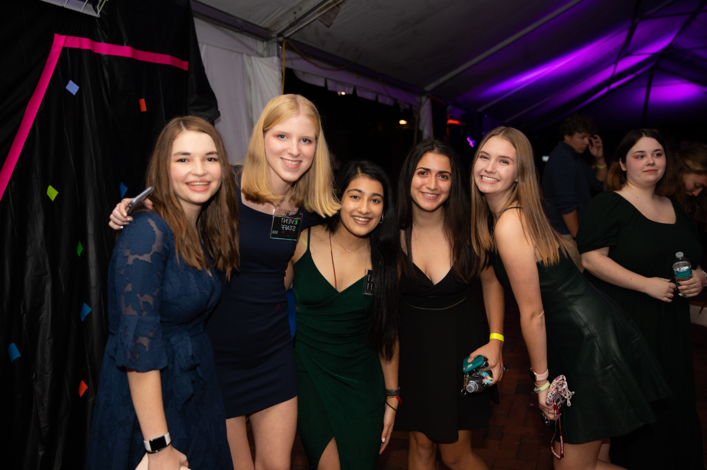 Four people in formal wear pose and smile for the camera with party decorations behind them.