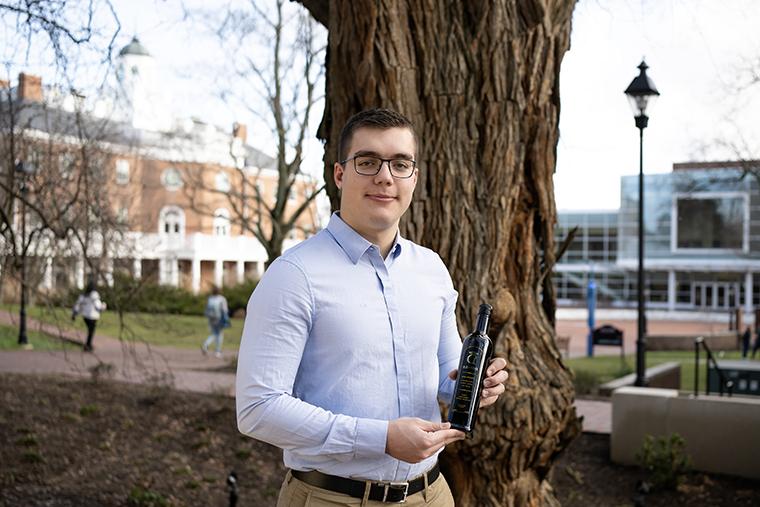 Bianti Danaj holds a bottle of his Donika橄榄油 in front of the Osage Orange tree on the library terrace